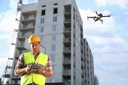 Builder operating drone with remote control at construction site. Aerial photography