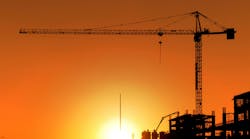 Construction Site and Crane. Horizontal photo of a construction site including a crane at sunset. The area is totally orange colored and all the buildings and equipment is seen as a silhouette