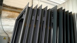 Stacked metal window frames with glass panes in workshop. Multiple dark gray metal window frames, complete with glass panes, are neatly stacked in a workshop environment