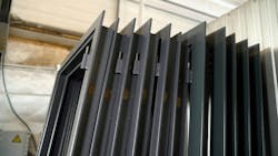 Stacked metal window frames with glass panes in workshop. Multiple dark gray metal window frames, complete with glass panes, are neatly stacked in a workshop environment Stacked metal window frames with glass panes in workshop. Multiple dark gray metal window frames, complete with glass panes, are neatly stacked in a workshop environment